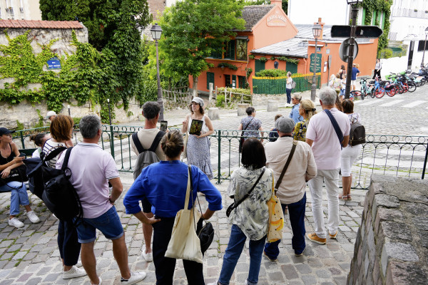 Anne-Sophie Guerrier com seu grupo de visitantes em frente ao cabaré Au Lapin Agile, mostrando o coelho desenhado por André Gill em seu tablet