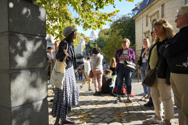 Anne-Sophie Guerrier contando una anécdota a sus visitantes junto al busto de Dalida en la Place Dalida, con la Rue de l’Abreuvoir al fondo y vista al Sacré-Cœur