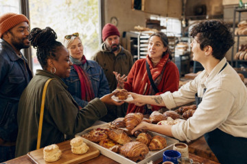A neighbourhood baker handing a fresh pastry to a guest while a small food-tour group gathers at the counter