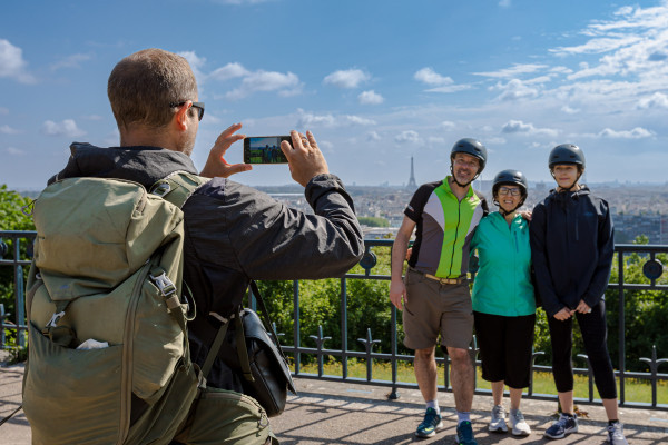 inaeri electric bike tour guide takes a picture of guests with a panoramic view of paris and eiffel tower in the background. located in parc de saint-cloud between paris and versailles
