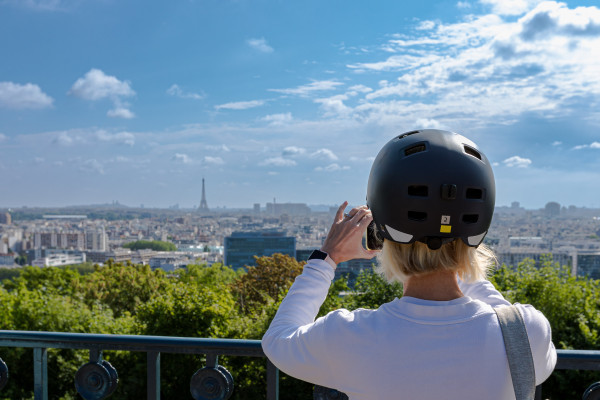 inaeri electric bike tour guest takes a picture of a panoramic view of paris and eiffel tower in the background. located in parc de saint-cloud between paris and versailles