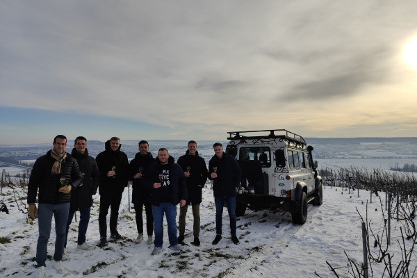 Champagne tasting on the mountain of the 1 cru snowy shared between seven friends, the sky is cloudy and yellow. They have their feet on the snow.