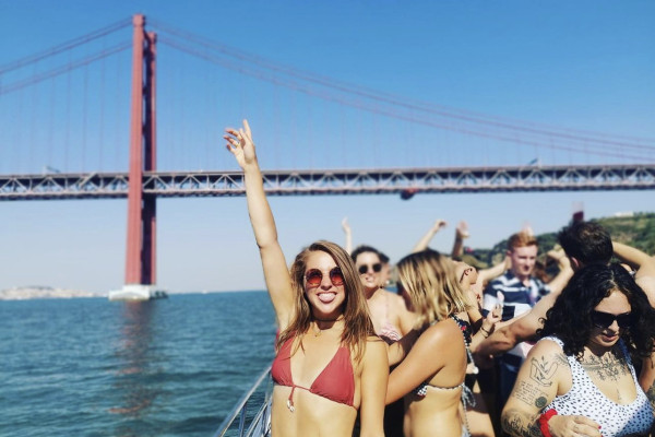 smilling women in bikini dancing on a boat party wth a group of friend, viewing the Lisbon's coastline