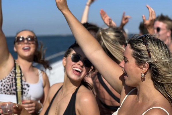 a group of people dancing, singing, smiling and waiving hands in the air on a boat party