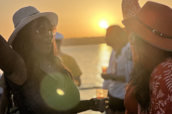 two beautiful ladies in stylish hats dancing in the light of the sunset on a dancefloor of a vibrant boat party