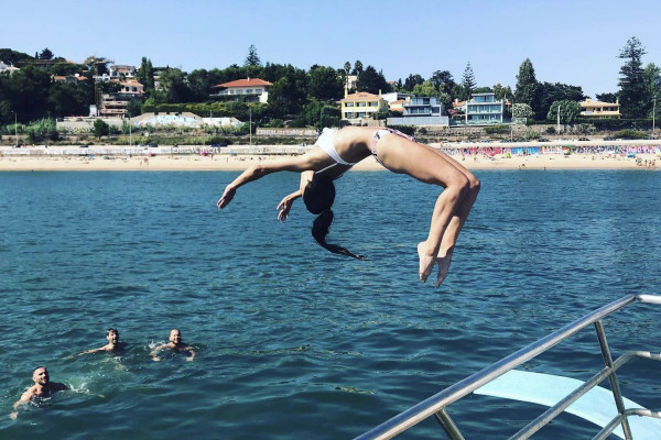 girl with brown hair in bikini jumping to the water from a jumping board on a boat making a backflip