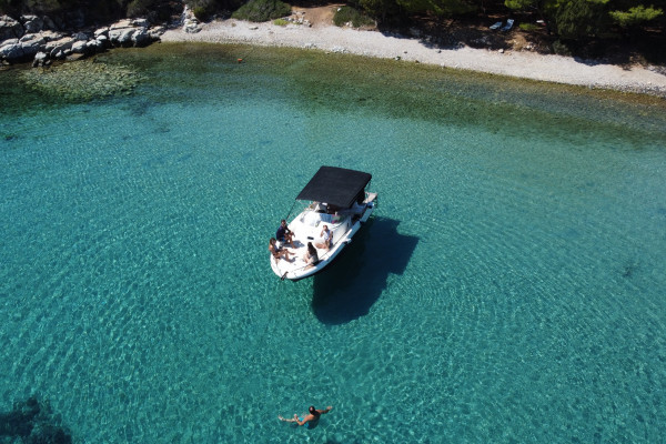 The boat is anchored in a bay during lunch time while people are swiming and enjoying the view.