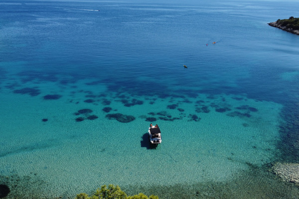 The boat is anchored in a bay during lunch time while people are swimming and enjoying the view.