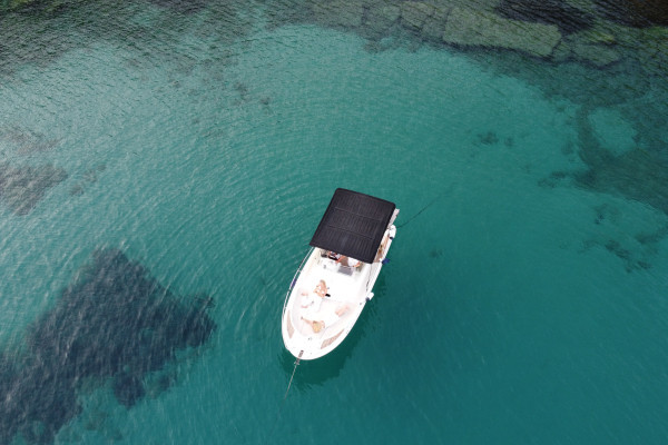 The boat is anchored in a bay during sunset time and two persons are laying in the front of the boat.
