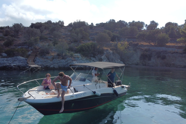 The boat is anchored in a bay during lunch time while people are laying in the front of the boat and are ready jump into the sea.
