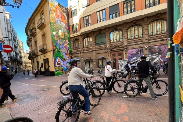 Cyclists stopping to view a tall, vibrant street art mural painted on a building façade