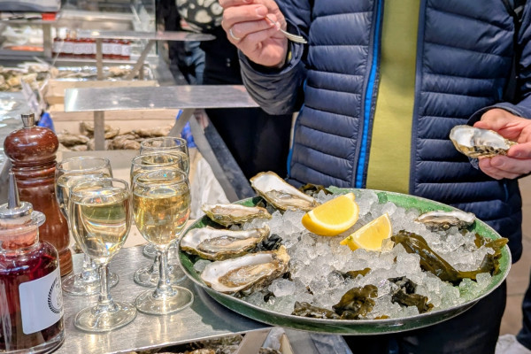 A tasting of seasonal seafood — shrimp and oysters — paired with a glass of local white wine during a Food Tour at Les Halles Paul Bocuse