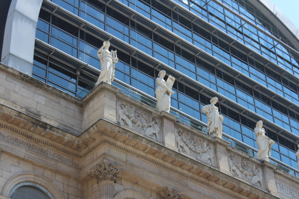 Photographie des muses de l'opéra de Lyon : 4 statues féminine sur le toit de l'édifice en pierre surplombé d'une grande verrière arrondie.