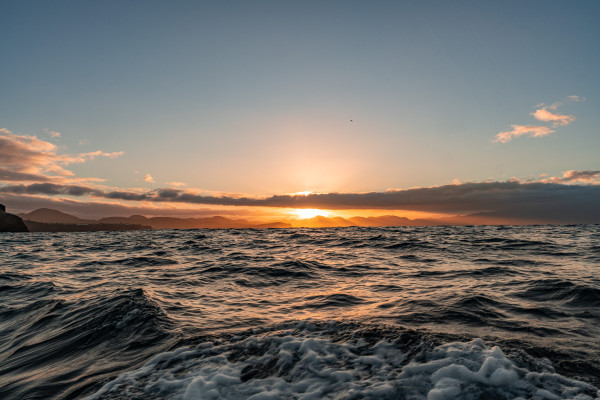alt="Coucher du soleil en pleine mer avec une vue unique de l’île"

